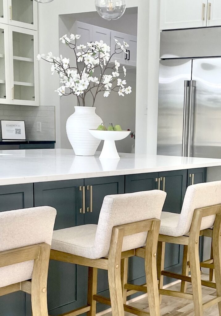 A kitchen island styled with a tall glass vase and long stems